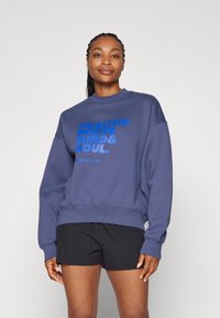 Mörkblå sweatshirt med rund hals och långa ärmar, prydd med fet blå text som står "HÄLSA & KROPP & SINNE & SÄL" framtill.