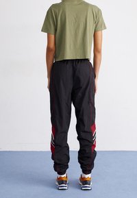 T-shirt vert olive court associé à un pantalon de jogging noir avec des bandes latérales rouges et des accents blancs, avec des poignets et une taille élastiques.