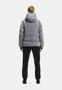 Szara pikowana kurtka z kapturem, o gładkiej fakturze i luźnym kroju, w połączeniu z czarnymi spodniami slim fit i butami turystycznymi.