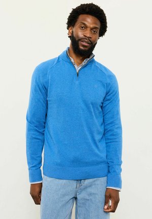 Blauer Strickpullover mit Reißverschluss am Kragen, gerippten Bündchen und Saum. Darunter ein Hemd mit leichtem Muster. Lässige Passform.