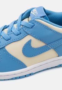 Niebieskie i beżowe trampki z gładkiej skóry, tekstylnymi sznurowadłami, logo Nike oraz białą gumową podeszwą z wzorzystym bieżnikiem.