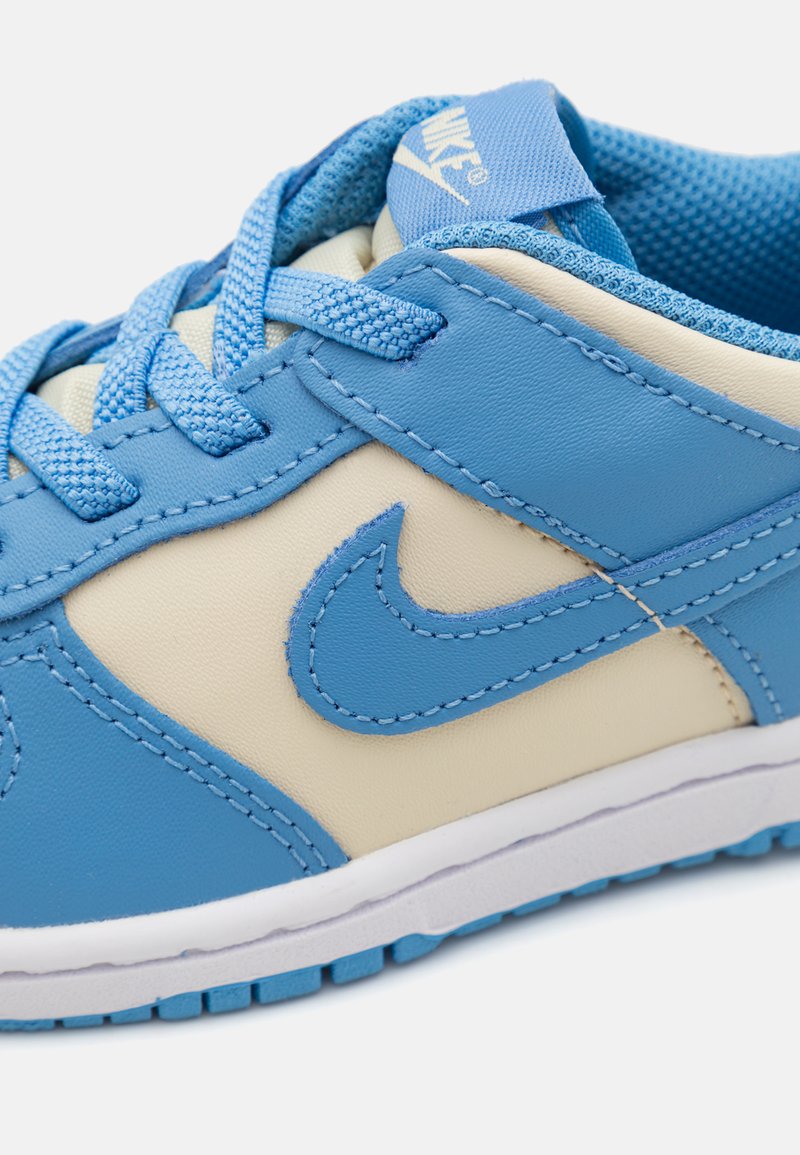 Blauwe en beige sneaker met een soepele leren bovenkant, getextureerde veters, Nike-logo en een witte rubberen zool met een gepatroniseerde loopvlak.