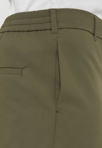 Κοντινό πλάνο στη μέση χακί παντελονιού με ελαστική πίσω μεριά, θηλιές για ζώνη, πλαϊνή τσέπη και ραφές ραμμένες με επιμέλεια.