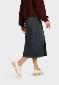 Gonna di jeans con lavaggio scuro, di media lunghezza, con spacco laterale, abbinata a scarpe chunky bianche con una fibbia decorativa. Taglio casual e rilassato.