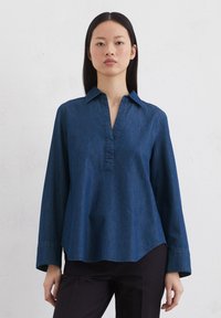 Tume sinine teksashirt sääreluudega krae, poolnupu sulgemisega ja pikkade varrukatega. Omab mugavat istuvust ja kumerat serva.