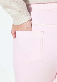 Vaaleanpunaiset farkkuhousut, joissa näkyvä takatasku. Kangas näyttää pehmeältä, yksityiskohtina saumurit ja kevyt tekstuuri, parina kermanvärinen neulehiha.