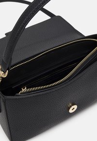 Svart strukturerad läderhandväska med guldzipper och magnetknapp, delvis öppen som visar inre fack och en handtag på toppen.