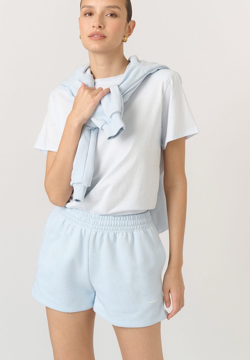 Jasnoniebieska bawełniana koszulka oraz pasujące szorty z elastycznym pasem. Jaśniejszy niebieski sweter jest narzucony na ramionach. Gładka faktura.