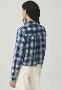 Blauw-witte geruite blouse met lange mouwen, knopen bij de manchetten en een casual kraag. Zacht materiaal met een ontspannen pasvorm en een rugplooidetail.