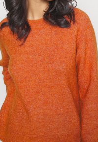 Pomarańczowy dziany sweter z okrągłym dekoltem i długimi rękawami. Miękki, teksturowany materiał o lekko luźnym kroju.