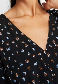 Robe florale noire avec un décolleté en V, petits motifs floraux bleus et marron, et boutons sur le devant. Tissu doux avec une texture délicate.