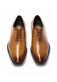 Brown leather dress shoes with a smooth finish, pointed toe, six eyelets, and a thin black sole. Branding visible inside the shoe.
