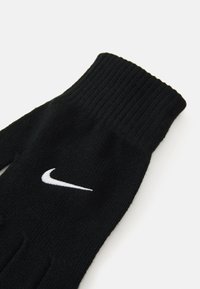 Fekete kötött kesztyű, fehér Nike swoosh logóval a hátán, fehér háttéren elszigetelve.