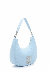 Sac à main matelassé bleu clair avec une seule bandoulière, une fermeture éclair argentée et une plaque logo en métal à l'avant.