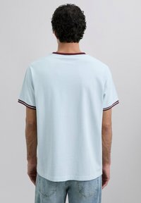 Camiseta de manga corta azul claro con ribete burdeos alrededor del cuello y las mangas, con una textura suave y un corte relajado.