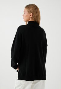 Czarny, oversize sweter z wysokim kołnierzem i prążkowanymi mankietami. Wykonany z miękkiego materiału, charakteryzuje się luźnym krojem i swobodnym designem.