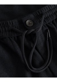 Jogging en polaire noire avec taille à cordon, finition élastique et accent de bouton. Le tissu semble doux avec une texture finie.