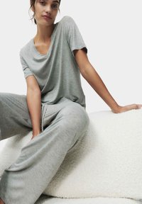 Lyst grå loungewear sæt bestående af en afslappet V-hals T-shirt og brede bukser, lavet af blødt, let stof. Tekstureret hvid baggrund.