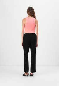 Un haut sans manches rose associé à un pantalon noir ample. Le tissu semble lisse ; le pantalon a une taille élastique.