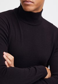 Suéter negro de cuello alto hecho de un suave tejido de punto, con un cuello acanalado y mangas ajustadas, que presenta un diseño sin costuras.