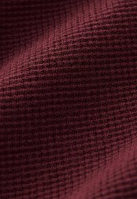 Tissu en maille bourgogne avec un motif texturé, présentant un design en grille et une surface douce, légèrement surélevée pour plus de profondeur et de dimension.