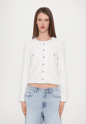 White, textured cropped jacket with a round neckline, front pockets, and silver buttons. Paired with light blue denim jeans.