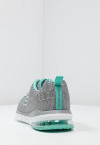 Grå och teal Skechers-sneakers med stickad tyg, dragflik och synlig luftkudde-sula, visad från baksidan på en vit yta.