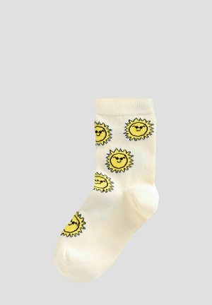 Chaussettes jaunes à motif soleil, faites de tissu doux, avec un fond crème clair et une bordure côtelée, présentant des designs de soleils souriants.