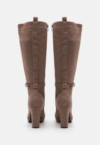 Hnědé semišové vysoké kozačky s robustním podpatkem, se zipem na vnější straně a ozdobným páskem blízko vršku.