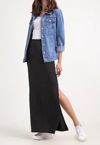 Farkkutakki nappiyksityiskohdilla, valkoinen vartalonmyötäinen T-paita, pitkä musta hame, jossa on sivuaukko, yhdistettynä valkoisiin tennareihin. Rennon asun esittely.