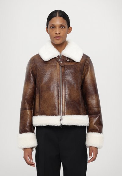 Braune Lederjacke mit weißem Lammfellkragen und -manschetten, ausgestattet mit einem Frontreißverschluss und Schnallendetails, im taillierten Design.