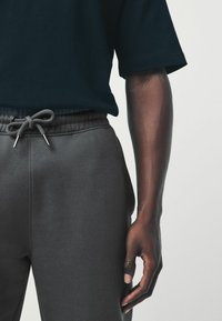 Black cotton t-shirt with short sleeves and gray sweatpants featuring a drawstring waist. Smooth texture, relaxed fit, and no visible patterns.