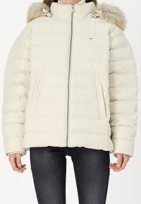 Cremefarvet dynejakke med pelsforet hætte, der har en frontlynlås, to sidelommer og et quiltet design. Blød tekstur, varm isolering.