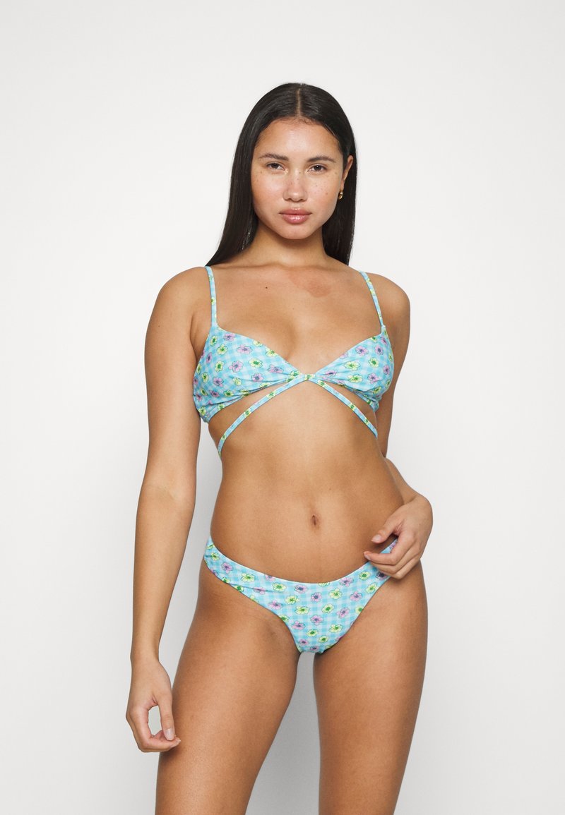 Conjunto de bikini em azul claro com padrões florais, apresentando um top triangular com alças cruzadas e uma parte debaixo de cintura baixa, feito de um tecido suave.