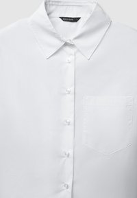 Chemise blanche à boutons avec col pointu et poche poitrine gauche, boutons sur le devant, taille étiquetée petite.