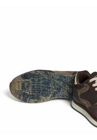 Brown and beige sneaker with worn, patterned sole lying on its side against a white background.