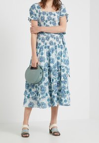 Blå och vit blommönstrad klänning med volangskikt, korta puffärmar och fyrkantig halsringning. Accessoarer med en rund teal-färgad handväska.