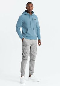 Sudadera azul claro con un bolsillo frontal y cordón ajustable, combinada con pantalones cargo gris claro con bolsillos laterales y zapatillas blancas.