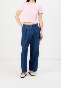 Camiseta corta de color rosa claro con un diseño sutil, combinada con jeans de mezclilla azul de tiro alto y pierna ancha, y zapatos color crema.
