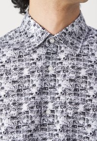 Skjorta med krage i svart och vitt, med ett upprepat grafiskt mönster av rektangulära former; tillverkad av lätt tyg med knappar.