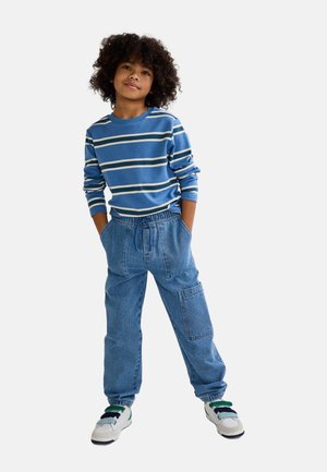 Chemise à manches longues à rayures bleues avec des rayures blanches et marine, associée à un pantalon en denim ample doté d'une poche cargo et d'une taille élastique.