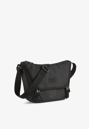 Fekete keresztpántos táska tartós anyagból, vörös varrással, állítható pánttal, fedélzárral és logó matricával.