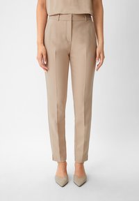 Beżowe, dopasowane spodnie z płaskim przodem, posiadające boczne kieszenie i rozcięcia na dole, w zestawie z jasnoszarymi, spiczastymi szpilkami.