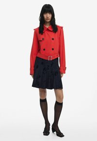 Red double-breasted jacket with a collar and belt, paired with a navy floral pleated skirt and black thigh-high stockings, featuring heeled shoes.