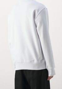 Vit sweatshirt med långa ärmar, rundad halsringning och ribbade manschetter. Mjuk tyg med en slät yta. Bärs med svarta byxor, synlig detalj på ryggen.