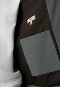 Szary kieszeń na ciemnoniebieskim materiale z widoczną białą koszulą. Metka z napisem "NEXT", rozmiar M. Tkanina wydaje się gładka z czystymi szwami.