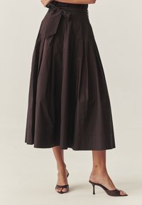 Braune plissierte Mid einrock mit einem gebundenen Taillenbund, aus glattem Stoff gefertigt, mit ausgestellter Form und sauberem Saum, kombiniert mit offenen Absatzschuhen.