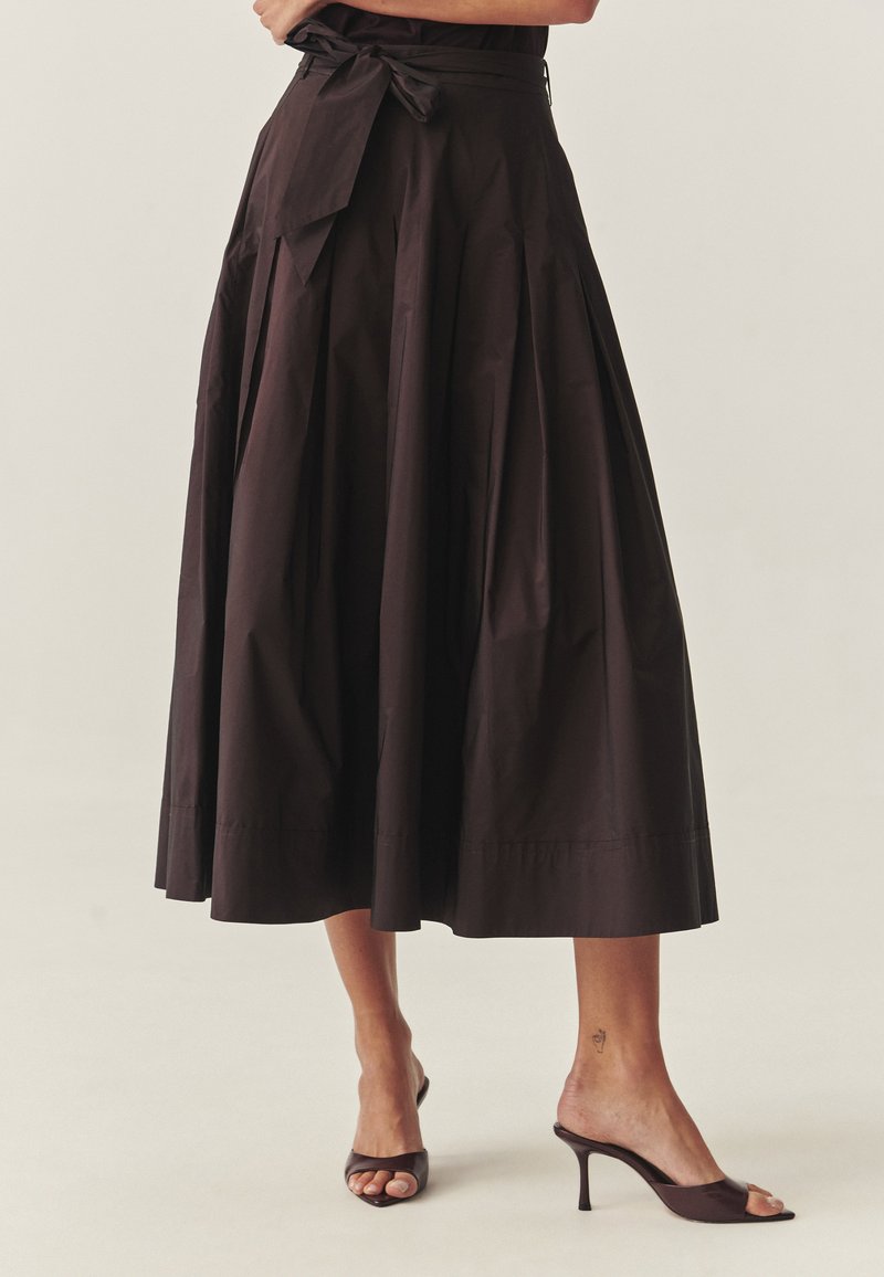 Braune plissierte Mid einrock mit einem gebundenen Taillenbund, aus glattem Stoff gefertigt, mit ausgestellter Form und sauberem Saum, kombiniert mit offenen Absatzschuhen.