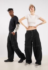Black cargo pants with white stitching, featuring multiple pockets. The cropped white top is paired with a black t-shirt and various sneakers.