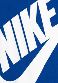 T-shirt in cotone blu con grande logo bianco "NIKE" e design a forma di swoosh. Texture liscia con tipografia audace.